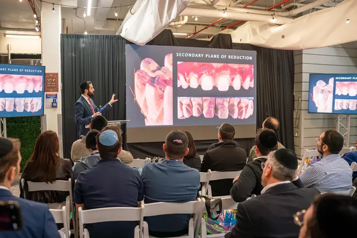 Speaker presenting a dental CE lecture on secondary plane of reduction to a seated audience