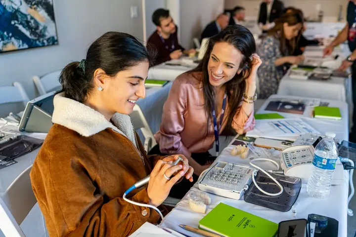 Two women laughing during a hands-on dental workshop with dental models and instruments on the table