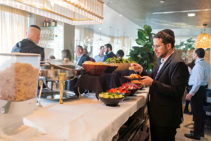 Attendee serving himself at a glatt kosher conference lunch buffet with salads and hot dishes
