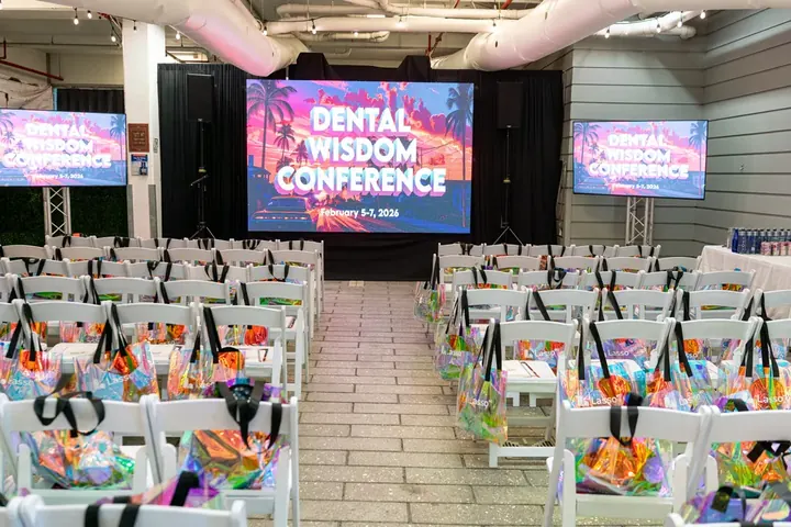 Conference room set up with rows of white chairs, holographic gift bags, and Dental Wisdom Conference on the main screen