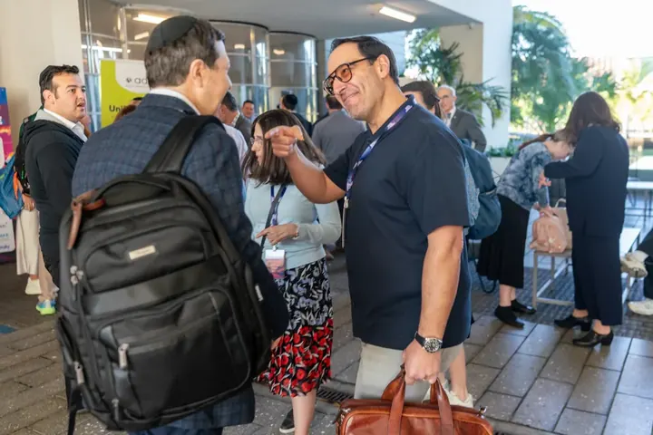 Attendees greeting each other outside the conference venue surrounded by palm trees and sunshine