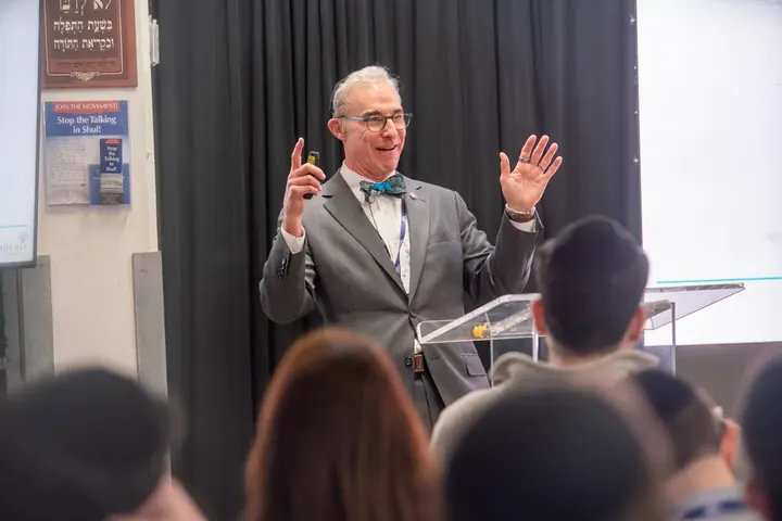 Conference speaker in a bow tie gesturing expressively at the podium during a CE lecture