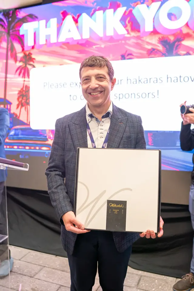 Attendee smiling and holding a framed sponsor appreciation gift in front of a Thank You slide