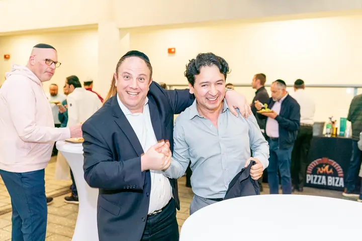 Two attendees laughing together at an evening social event with Pizza Biza branding visible in the background