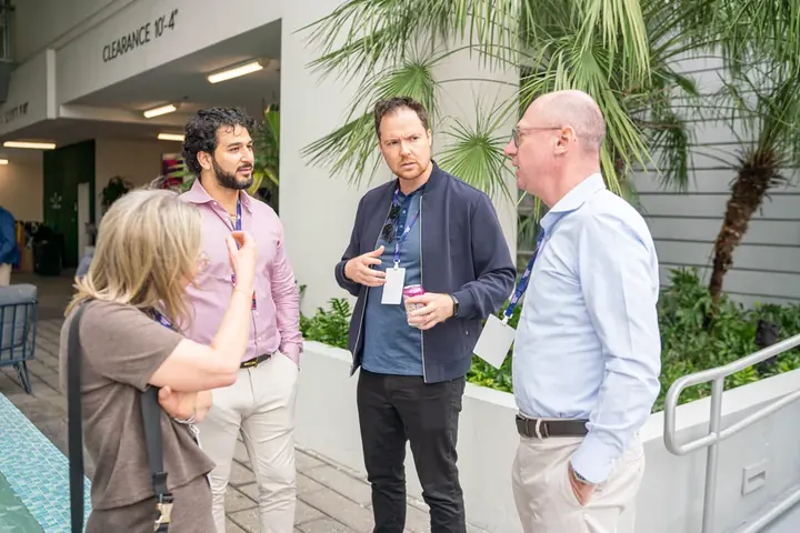 Small group of conference attendees networking outdoors near palm trees