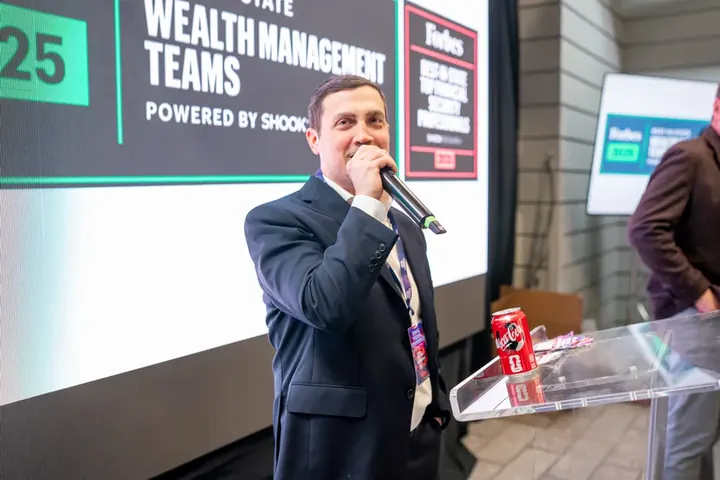 Speaker presenting at a microphone in front of a wealth management presentation slide